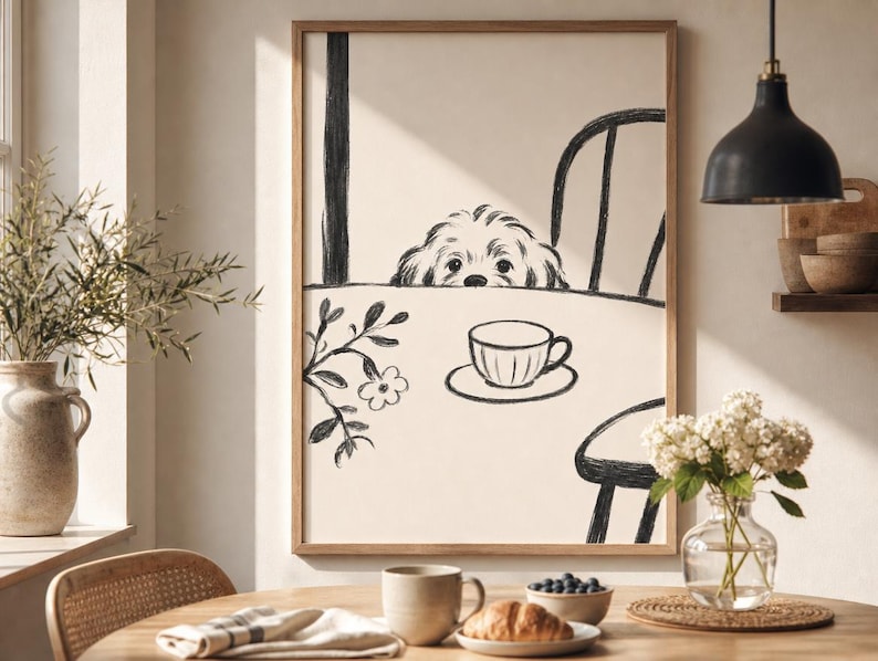 May include: A framed art print featuring a black and white sketch of a dog peeking over a table with a teacup. The artwork is in a wooden frame and is displayed in a well-lit room with a table set for breakfast.