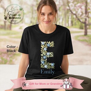 May include: Black t-shirt with a floral letter "E" design and the name "Emily" in blue. The design includes blue flowers and green leaves. The shirt is a gift for Mom or Grandma.