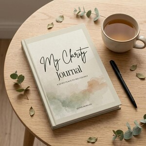 May include: A hardback journal, "My Clarity Journal", with a watercolour design and the text "A quiet place to see clearly." A black pen and a cup of tea are on a wooden table. The author's name, Quinn Morgan, is at the bottom of the journal.