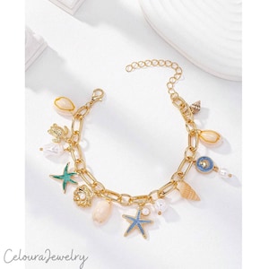Könnte beinhalten: Ein goldfarbenes Gliederkettenarmband mit verschiedenen nautischen Anhängern, darunter eine Meeresschildkröte, Seesterne in blauem und grünem Emaille, verschiedene Muscheln und kleine weiße Perlen. Das Armband hat eine verstellbare Verlängerungskette.