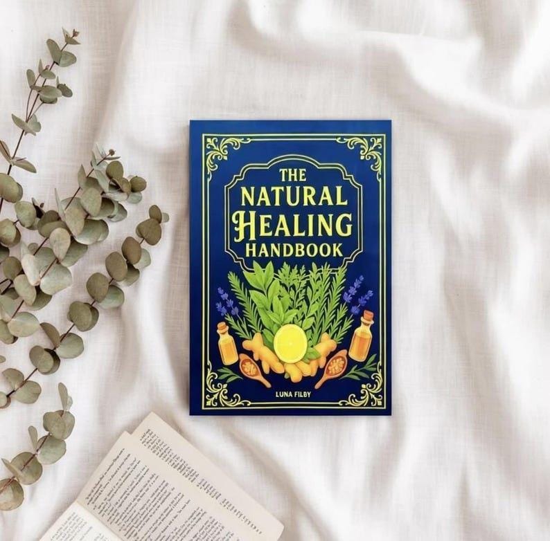 Peut inclure: Un livre &agrave; couverture rigide bleu marine intitul&eacute; "The Natural Healing Handbook" avec des lettres dor&eacute;es. La couverture pr&eacute;sente des illustrations d'herbes, d'huiles essentielles et d'un citron. Le livre est pos&eacute; sur une surface blanche textur&eacute;e.
