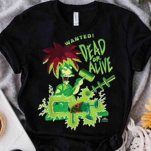 May include: A black short-sleeved t-shirt featuring a graphic print of a cartoon character with spiky red hair holding a mallet over another character. The text reads WANTED! DEAD OR ALIVE in bright green letters against a black background.