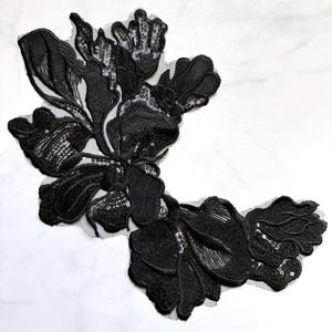 May include: Black floral lace applique with sequin accents. The applique features a detailed design of leaves and petals, perfect for embellishing garments or accessories. The intricate embroidery and shimmering sequins add a touch of elegance and sophistication to any project.