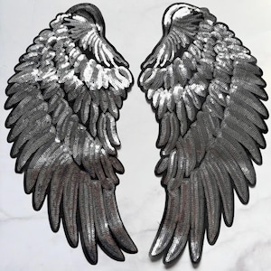 May include: Two matching decorative angel wing patches. Each wing is black with silver sequins, creating a shimmering effect. The wings are designed with detailed feather patterns and are likely for clothing or craft projects.