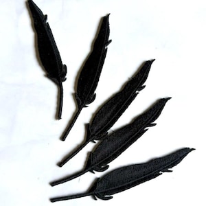 May include: Five black embroidered feather patches arranged in a fan-like pattern. Each patch features a detailed stitched texture with a central quill and fine, thread-like barbs extending outward, creating a realistic silhouette of a bird feather.