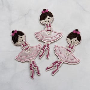 Puede incluir: Tres parches bordados que muestran una bailarina con cabello castaño oscuro, un lazo rosa en el pelo y un vestido de tutú rosa claro. Cada figura aparece en una pose de baile con zapatillas de ballet rosas y cintas en piernas y pies.