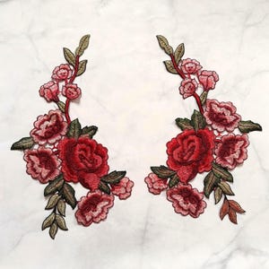 May include: Two symmetrical floral embroidery patches featuring deep red roses and smaller pink blossoms with olive green leaves and stems. The intricate threadwork creates a detailed botanical design with varied shades of red, pink, and green.