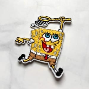 May include: Embroidered patch featuring the animated character SpongeBob SquarePants in a running pose, holding a net. The patch is yellow, brown, white, and black, with blue eyes and a red mouth. The patch is approximately 3 inches tall.