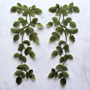 Puede incluir: Dos diseños de vid con hojas verdes bordadas sobre un fondo blanco. Los diseños presentan hojas y tallos detallados, perfectos para embellecer ropa o manualidades. Las hojas tienen un aspecto texturizado.