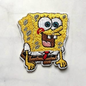 May include: Embroidered patch featuring the cartoon character SpongeBob SquarePants. The patch is yellow with a white border, and depicts SpongeBob with his tongue sticking out. He is wearing a white shirt, brown pants, and a red tie.