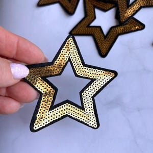 Può includere: Toppe a forma di stella con paillettes dorate e bordi neri. Le toppe a forma di stella hanno un centro vuoto e sono impreziosite da paillettes dorate lucenti. Ideali per aggiungere un tocco di brillantezza a vestiti o accessori.
