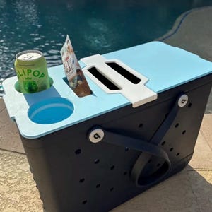 May include: A white ceramic mug with a black handle and the text "But First, Coffee" in a bold, black font. The mug is set against a blurred background, suggesting a cozy setting.