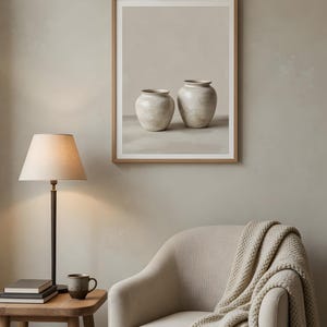 Peut inclure: Une impression d'art murale encadrée représentant deux vases en céramique beige, exposée au-dessus d'un fauteuil beige drapé d'un plaid en tricot texturé, d'une table d'appoint en bois avec une lampe, de livres et d'une petite tasse en céramique.