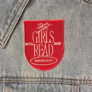 May include: A light blue denim vest featuring a red shield-shaped patch with white embroidered text that reads Hot GIRLS READ ESTD 2026 BOOKCLUB. The vest has a classic collar, metal buttons, and a chest pocket with a button closure.