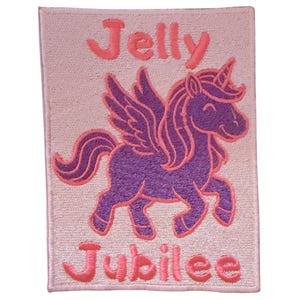 Op de afbeelding: Geborduurde patch met een paarse gevleugelde eenhoorn, roze manen, hoorn en accenten. De patch heeft de tekst "Jelly Jubilee" in roze script. De achtergrond is lichtroze. Ideaal voor kleding of accessoires.