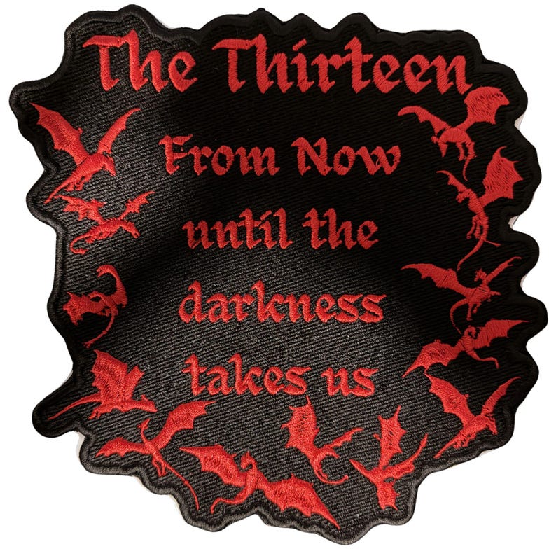 Peut inclure: Un &eacute;cusson brod&eacute; noir &agrave; bord irr&eacute;gulier avec du texte rouge indiquant The Thirteen From Now until the darkness takes us. Le motif est entour&eacute; de plusieurs petites silhouettes de dragons rouges dans diverses postures de vol.