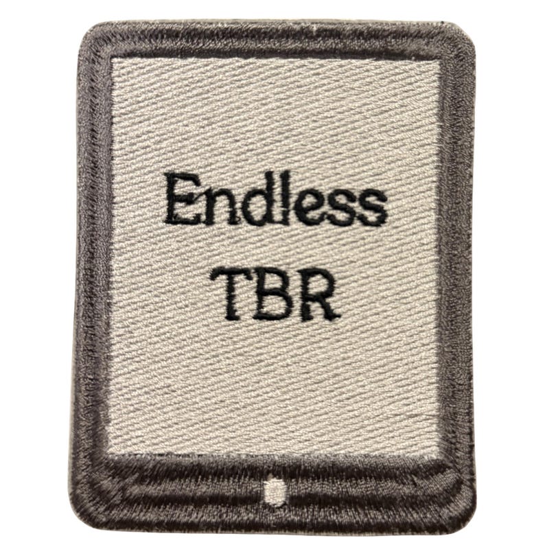May include: A rectangular embroidered patch featuring a light gray center with a dark gray border. The text "Endless TBR" is stitched in black thread in the center. The design resembles an e-reader device with a small button at the bottom.