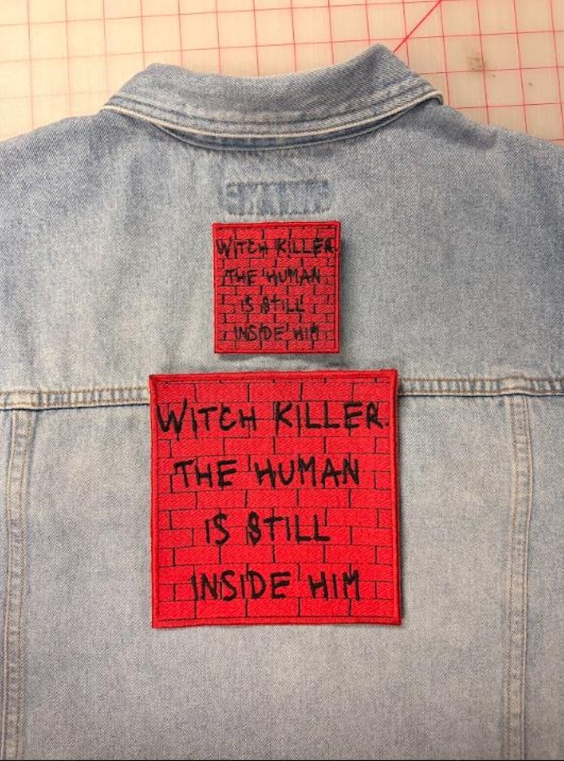 May include: A light blue denim jacket featuring two square red patches with a black brick pattern and the black embroidered text: WITCH KILLER. THE HUMAN IS STILL INSIDE HIM. The patches are positioned vertically on the back of the jacket.