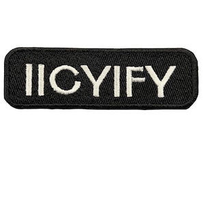Może przedstawiać: Prostokątna haftowana naszywka z czarnym tłem i zaokrąglonymi rogami. Napis IICYIFY jest wyhaftowany białą nicią na środku naszywki bezszeryfową czcionką. Krawędzie są wykończone czarnym obszyciem.