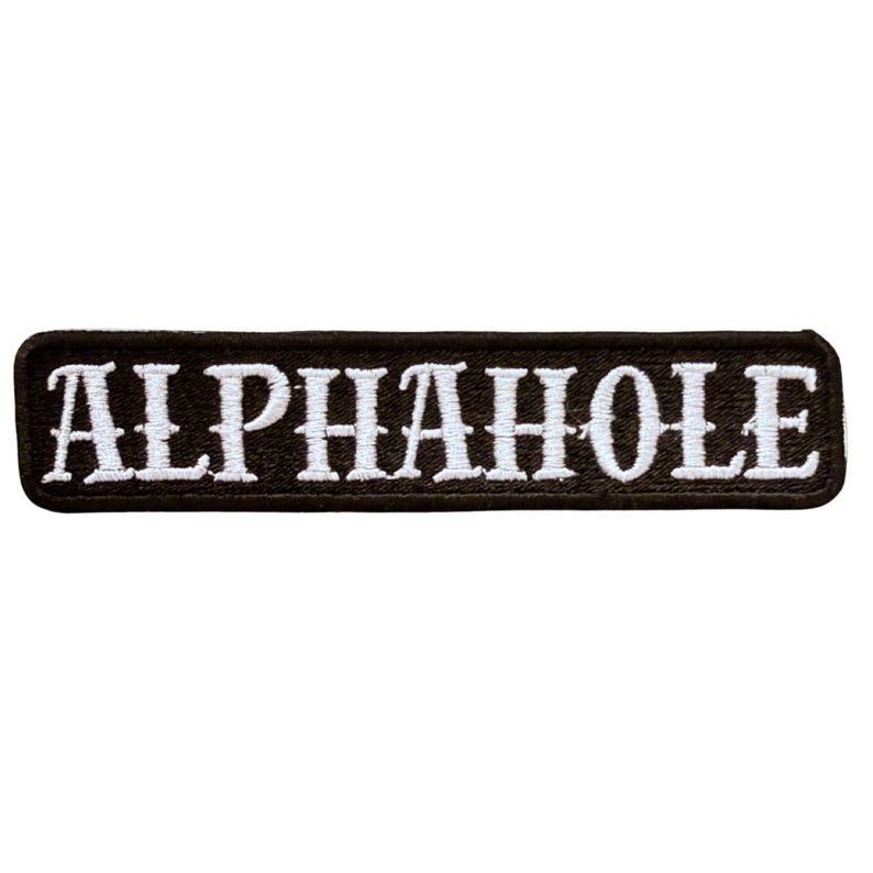K&ouml;nnte beinhalten: Ein rechteckiger bestickter Aufn&auml;her mit schwarzem Hintergrund und wei&szlig;em Rand. Das Wort ALPHAHOLE ist in wei&szlig;en Gro&szlig;buchstaben in der Mitte des Aufn&auml;hers eingestickt. Der Text zeigt einen fetten Serifenschriftstil mit sauberen, scharfen Kanten.