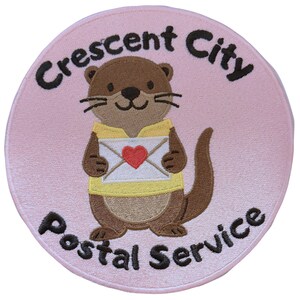 May include: Embroidered patch featuring a cartoon otter holding an envelope with a red heart. The otter wears a yellow shirt and is set against a light pink background. The text "Crescent City Postal Service" is arched around the design.