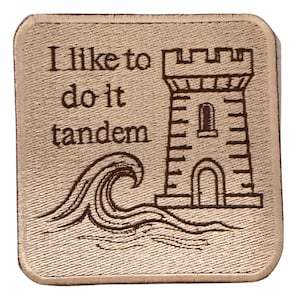 Peut inclure: Écusson carré beige avec texte et images brodés. Le texte se lit « J'aime le faire en tandem ». Une tour de château et des vagues océaniques sont également brodées sur l'écusson. L'écusson a une bordure cousue.