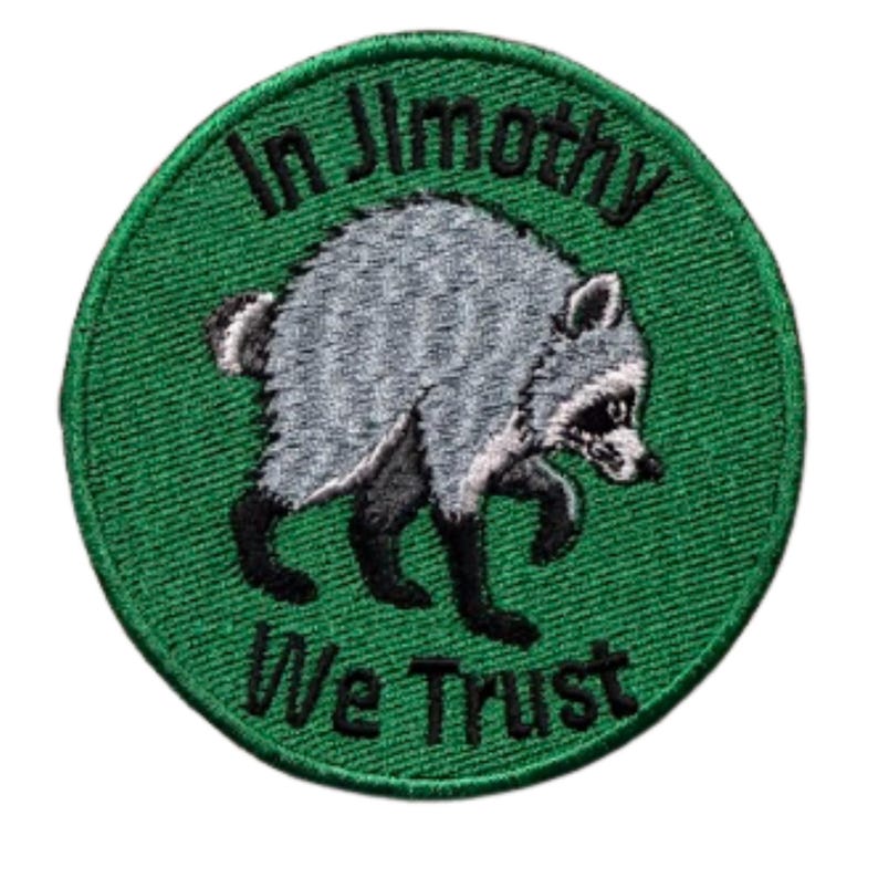 May include: A circular embroidered patch with a green background featuring a grey and black raccoon in the center. The text "In Jimothy" is arched above the raccoon, and the text "We Trust" is arched below, both in black embroidered lettering.