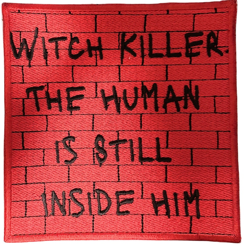 May include: A square embroidered patch featuring a red brick wall pattern with black stitching. The text WITCH KILLER. THE HUMAN IS STILL INSIDE HIM is embroidered in black thread across the center of the red brick background.