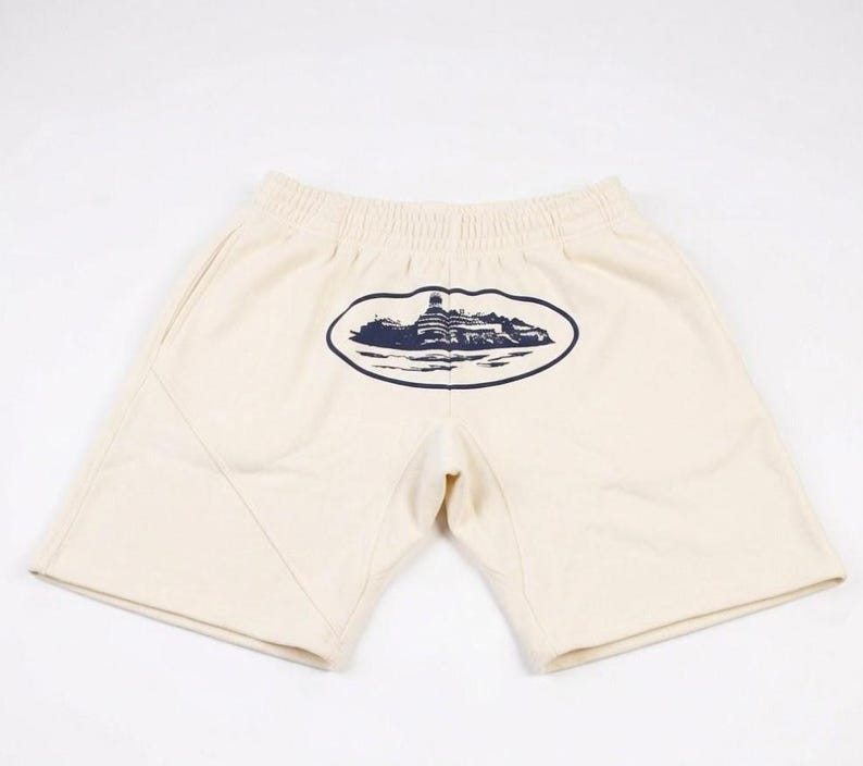 Może przedstawiać: Biały ceramiczny kubek z czarnym uchwytem i napisem "But First, Coffee" pogrubioną, czarną czcionką. Kubek jest ustawiony na rozmytym tle, sugerującym przytulne otoczenie.