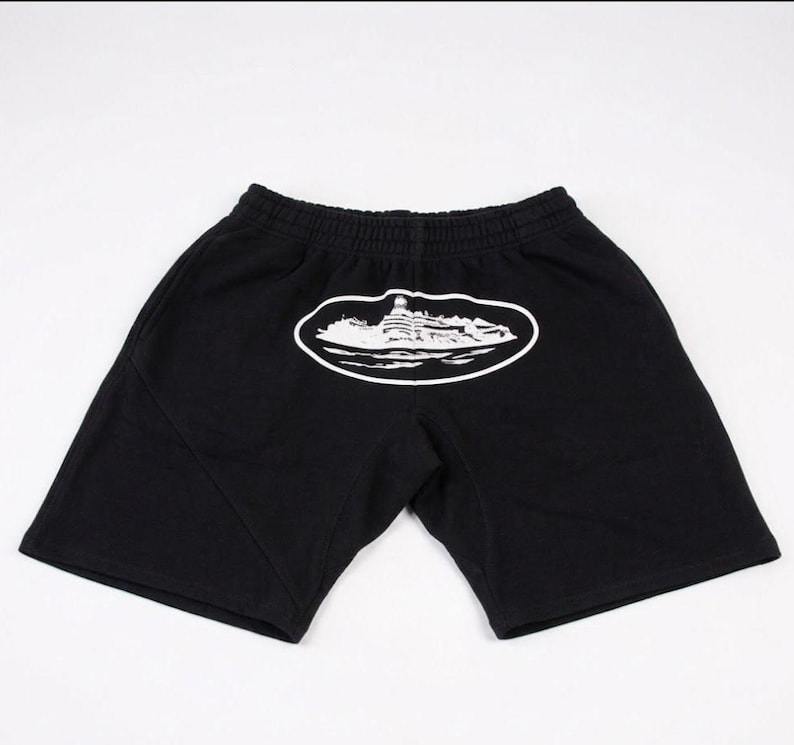 Może przedstawiać: Czarne szorty z elastyczną talią. Biała grafika budynku jest wyśrodkowana na plecach, w owalnym obrysie. Szorty wykonane są z miękkiego materiału.