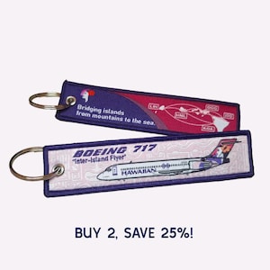 May include: Two rectangular fabric keychains with metal rings. One features a Hawaiian Airlines Boeing 717 with the text 'BOEING 717 Inter-Island Flyer'. The other shows a map of Hawaiian islands with the text 'Bridging islands from mountains to the sea.'