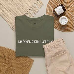 Puede incluir: Una camiseta de cuello redondo color verde oliva con el texto blanco ABSOFUCKINLUTELY impreso en una fuente estilo plantilla en el pecho. La prenda tiene mangas cortas y un corte estándar, con la etiqueta de la marca visible en el cuello.