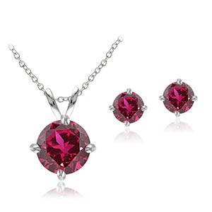 Puede incluir: Un conjunto de joyas con un collar de plata con un colgante redondo rojo intenso y pendientes a juego. El colgante y los pendientes tienen un engaste de cuatro puntas, y la cadena es delicada.