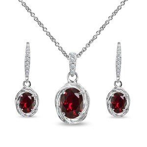Könnte beinhalten: Ein Schmuckset mit einer silbernen Halskette mit Anhänger und passenden Ohrringen. Jedes Stück zeigt einen großen, oval geformten, tiefroten Edelstein, der von einem silbernen Wirbeldesign umgeben und mit kleinen, funkelnden Steinen akzentuiert ist.
