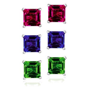 May include: Six square-cut gemstone stud earrings in three colors: ruby red, sapphire blue, and emerald green. Each pair of earrings is set in a silver-colored metal. The gemstones have a faceted appearance, reflecting light.