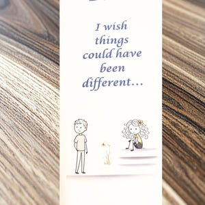 May include: A white card with the word "Dad" in a cursive font. The card reads "I wish things could have been different..." with illustrations of a boy, a flower, and a girl. The card is on a wooden surface.