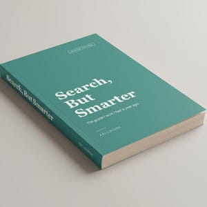 May include: A teal-colored book titled "Search, But Smarter" with white lettering. The book's cover also includes the subtitle "The guide I wish I had a year ago" and the author's name. The book is on a light gray surface.