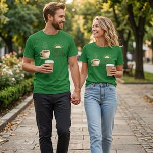 K&ouml;nnte beinhalten: Zwei Personen tragen passende gr&uuml;ne T-Shirts mit dem Aufdruck "Coffee & Sunshine". Die Shirts zeigen eine Kaffeetasse und eine Sonnengrafik. Sie halten H&auml;ndchen und gehen einen Weg entlang, jeder h&auml;lt einen Kaffeebecher.