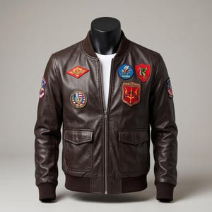 Puede incluir: Una chaqueta bomber de cuero marrón oscuro con cremallera frontal, puños y dobladillo acanalados, y dos bolsillos delanteros con solapa. La chaqueta está decorada con varios parches bordados, incluyendo un diamante rojo, un parche circular azul y un escudo.