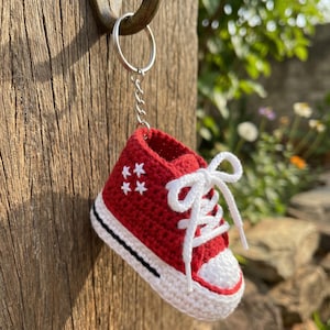 Peut inclure: Un porte-clés en forme de basket crochetée rouge avec des lacets blancs, un bout blanc et une semelle blanche ornée d'une fine rayure noire. Le côté de la chaussure rouge est décoré de quatre petites étoiles blanches brodées.