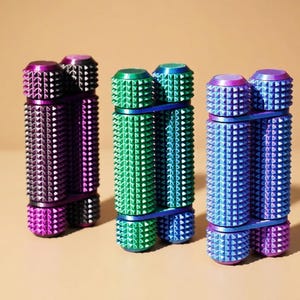May include: Three colorful, spiked massage rollers in purple, green, and blue. Each roller is composed of two cylindrical sections connected by a band. The rollers have a textured surface with evenly spaced, conical spikes.
