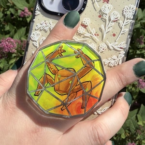 Peut inclure: Une coque de smartphone transparente avec un motif floral en lignes blanches et un support de téléphone circulaire. Le support présente une illustration géométrique de crabe doré, style vitrail, sur un fond jaune et orange vif.