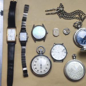 May include: A collection of vintage timepieces, including wristwatches with black leather and metal bands, pocket watches with silver cases, and a stopwatch. The watches feature various face designs and styles, showcasing a range of watchmaking aesthetics.