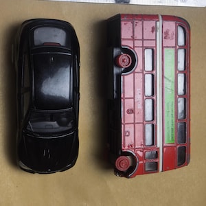 May include: A black toy car and a red double-decker bus are displayed. The bus has white window frames and the text "LONDON" and "You can get what you want". A ruler is placed above the toys.