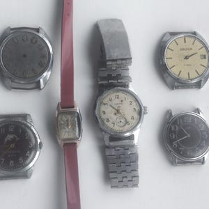 May include: A collection of vintage wristwatches with various face designs and metal bands. One watch has a red leather strap. The watch faces include black, cream, and silver tones. Some watches show the brand name SEKONDA.