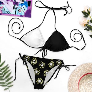May include: A two-piece bikini set. The top is a halter style with a white and black color block design. The bottoms are black with a repeating yellow skull and crossbones pattern. The bikini is tied with black strings.