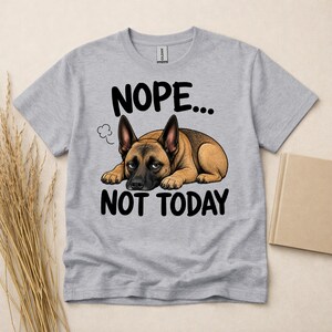May include: A light grey t-shirt featuring a graphic of a brown and black German Shepherd dog lying down with a tired expression. Above the dog is the text NOPE... and below the dog is the text NOT TODAY in bold black capital letters.