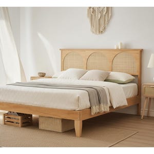 May include: A light wood bed frame with a woven headboard and matching nightstand. The bed is made up with white bedding and a gray throw blanket. A lamp with a white geometric base sits on the nightstand. A woven basket and wooden crate are under the bed.