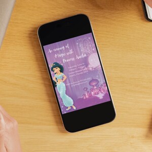 Op de afbeelding: Een smartphone toont een paarse uitnodiging met de tekst "An evening of Magic with Princess Amelia". De uitnodiging toont een cartoonprinses in een blauwe jurk en een kasteelillustratie. De telefoon ligt op een houten oppervlak.