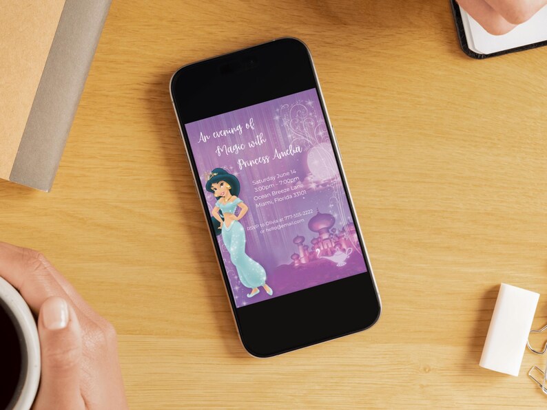 Op de afbeelding: Een smartphone toont een paarse uitnodiging met de tekst "An evening of Magic with Princess Amelia". De uitnodiging toont een cartoonprinses in een blauwe jurk en een kasteelillustratie. De telefoon ligt op een houten oppervlak.